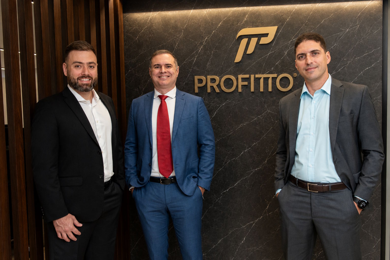 Três sócios da Profitto em frente à marca da empresa